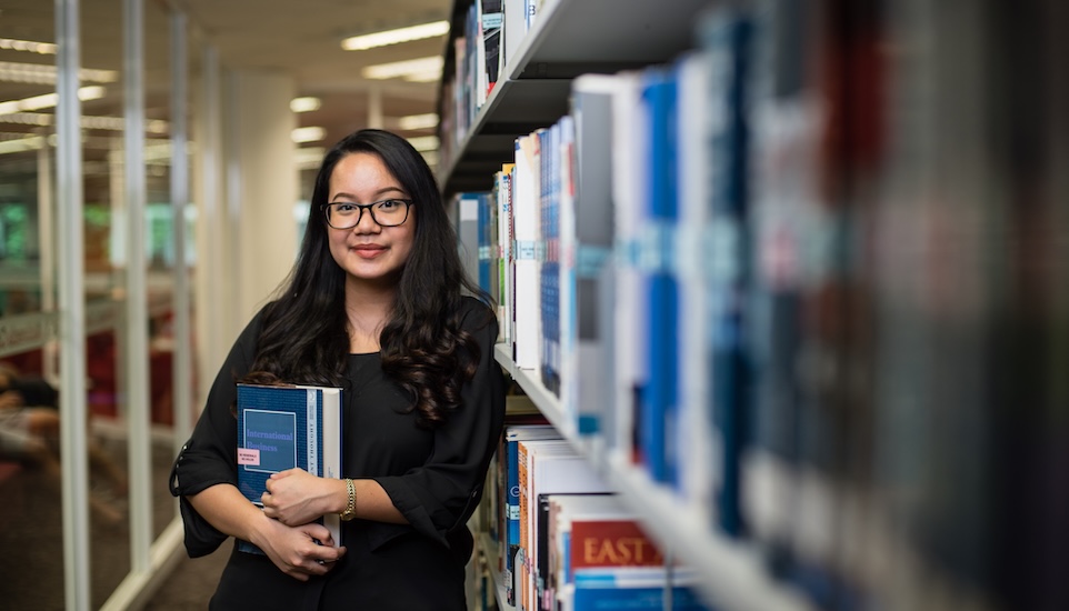 A Master's student holding a book in a library