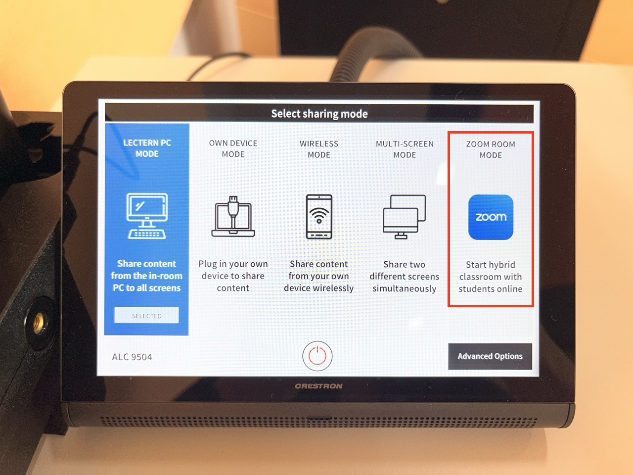 Crestron touch panel displaying a “Select sharing mode” screen in a hybrid classroom, showing options for Lectern PC, Own Device, Wireless, Multi-screen, and Zoom Room mode, with Zoom Room mode highlighted in a red box on the right.